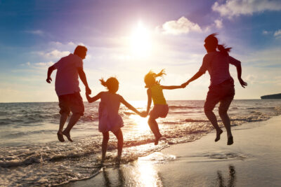 A family of four joyfully jumps on a beach at sunset, silhouetted against the sky. The ocean waves gently reach the shore, creating a serene and playful atmosphere that strengthens their bond with each leap, enhancing their family connection through shared activities.