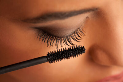 Close-up of a person applying black mascara to their eyelashes. The eye is closed, showcasing the best mascara for any busy girl's purse—ideal for a grab it & go mascara routine. The wand is held near the lashes, highlighting perfectly shaded eyelids and coated lashes.