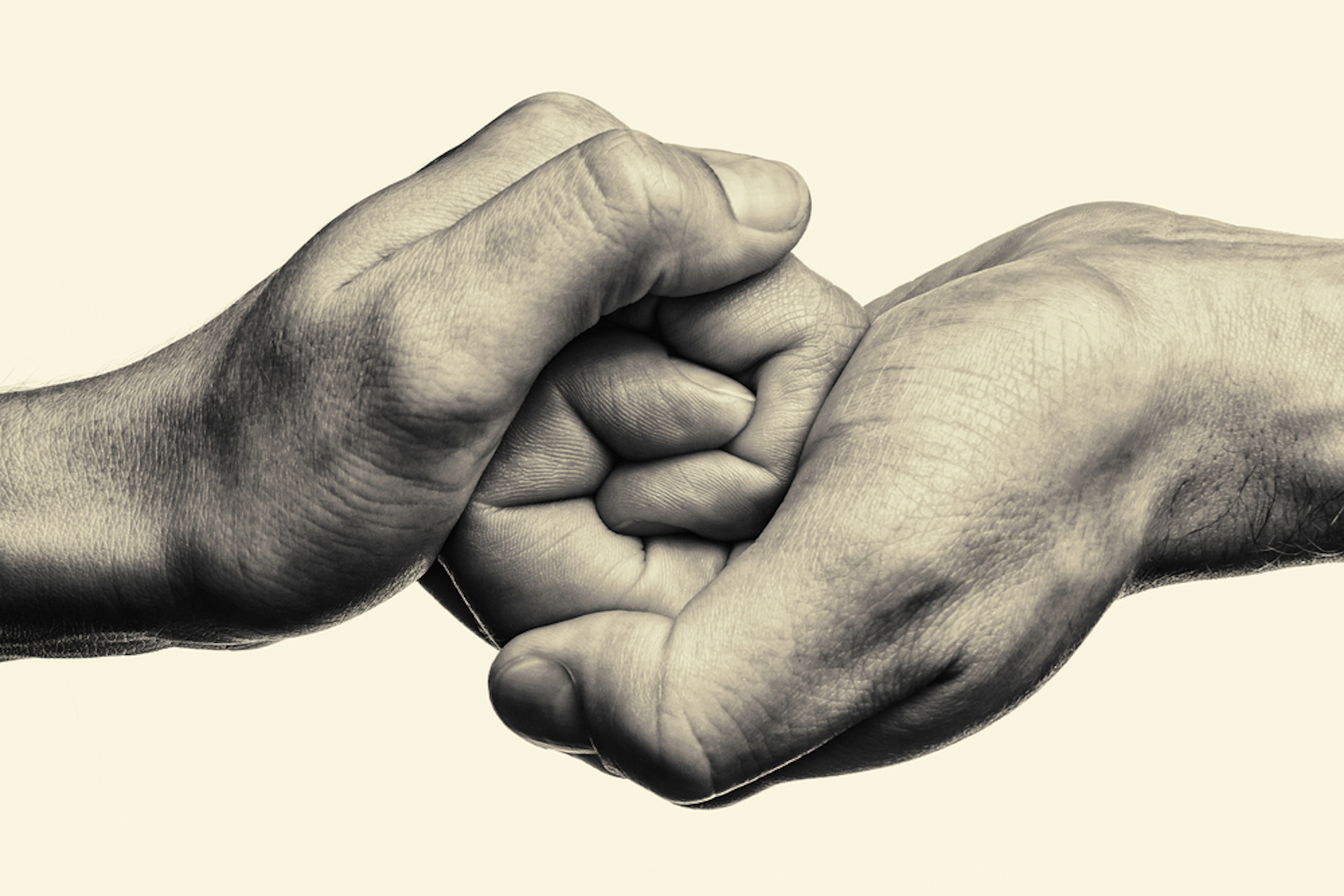 Two hands clasped together in a supportive gesture, with fingers interlocking to symbolize emotional intimacy. The black and white image highlights the textures and details of the skin, while the neutral background draws focus to the hands, emphasizing their deep connection.