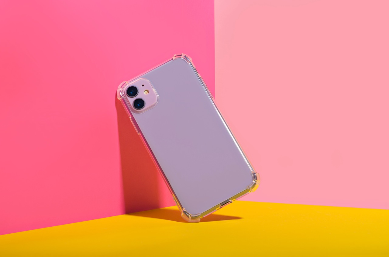 An iPhone with a clear case is placed diagonally against a vibrant background split between pink and yellow. The phone's dual cameras are visible on the upper corner, seamlessly integrating with the device's sleek design and iOS 17 features.